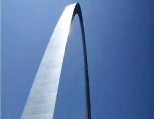 A polished steel arch soaring into a cloudless sky, sunlight catching its curved inner edge.