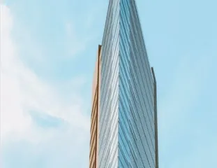 The glazed tower of the Grand Edelweiss Hotel tapering to a point, one bronze flank warm against a pale sky.