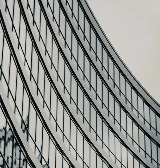 The curved glass facade of a high-rise, its banded windows sweeping away across a pale sky.