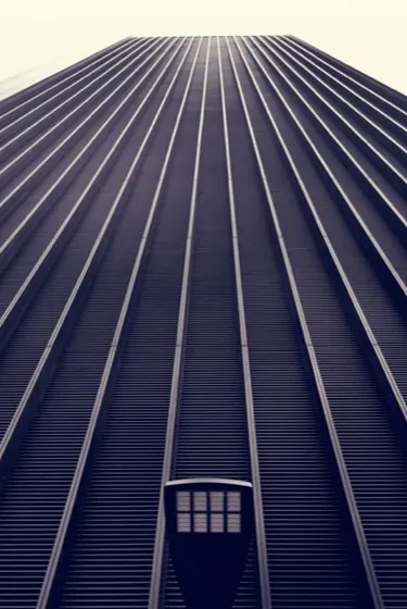 Looking up the deeply ribbed dark facade of Federal II Tower against a pale sky.