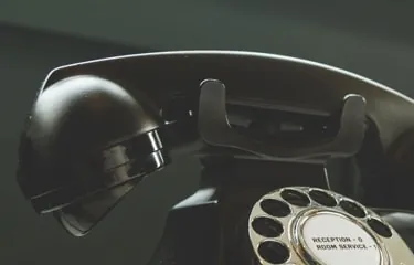 A black vintage rotary telephone on a desk, its dial labelled for reception and room service.