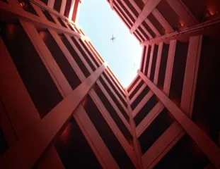 Red steel beams crossing overhead at Hypers, an aeroplane passing through the slice of bright sky between them.
