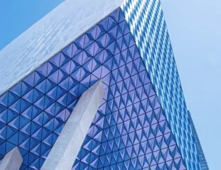 The triangulated blue glass skin of Project Paramour, its ridge catching the light against a clear sky.