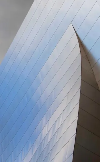 Two curved, steel-panelled walls of a building meeting at a knife-sharp edge under a pale sky.